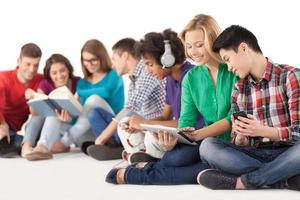 adolescentes despreocupados. grupo de estudantes multiétnicas a passar tempo juntos enquanto está sentado isolado no branco foto