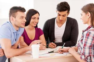 estudar juntos é divertido. quatro estudantes alegres estudando juntos enquanto estão sentados na mesa foto