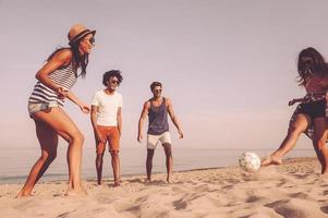 aproveitando o tempo com os amigos. grupo de jovens alegres brincando com bola de futebol na praia foto