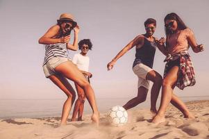 diversão na praia com os amigos. grupo de jovens alegres brincando com bola de futebol na praia foto