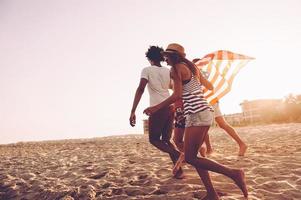 nascido para ser livre. alegres jovens carregando bandeira americana enquanto correm juntos na praia foto