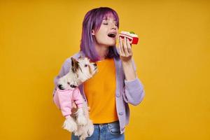 jovem alegre carregando cachorrinho e comendo bolo em pé contra um fundo amarelo foto