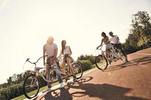 vida cheia de amizade. grupo de jovens modernos em roupas casuais sorrindo enquanto andam de bicicleta juntos ao ar livre foto