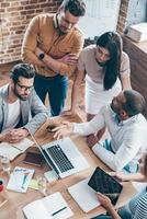 brainstorming criativo. parte da vista superior do grupo de cinco jovens discute algo e gesticula enquanto se inclina para a mesa no escritório foto