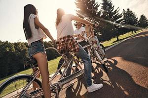 dia perfeito para um passeio de bicicleta. grupo de jovens felizes em roupas casuais sorrindo enquanto andam de bicicleta juntos ao ar livre foto