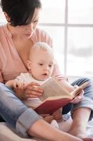 pequeno leitor de livros. jovem mãe segurando bebê e lendo um livro foto