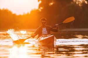 caiaque é seu estilo de vida. jovem confiante andando de caiaque no rio com pôr do sol ao fundo foto