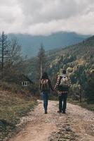 estrada longa. vista traseira de comprimento total do jovem casal de mãos dadas enquanto caminhava nas montanhas foto