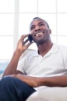 no telefone. alegre homem africano falando no celular e sorrindo enquanto está sentado na cadeira foto