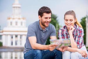 escolhendo o lugar para ir. feliz casal jovem turista sentado perto de belo edifício e examinando o mapa juntos foto