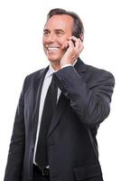 boa conversa de negócios. feliz homem maduro de camisa e gravata falando no celular e sorrindo em pé isolado no fundo branco foto