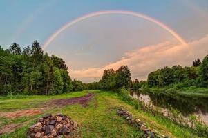 lindo arco-íris duplo sobre o rio com estrada suja ao longo foto