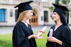 discutindo a cerimônia. duas jovens felizes em vestidos de formatura segurando diplomas e conversando foto