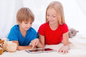 tecnologias tornam-se mais fáceis. duas crianças bonitas brincando no tablet digital e sorrindo enquanto estavam deitados juntos na cama foto