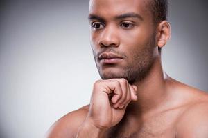 sonhador do dia. retrato de jovem africano segurando a mão no queixo e desviar o olhar em pé contra um fundo preto foto