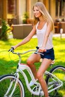 relaxando com sua bicicleta. bela jovem loira sorrindo enquanto andava de bicicleta ao ar livre foto