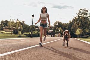 despreocupado e feliz. comprimento total de mulher jovem e bonita brincando com seu cachorro e sorrindo enquanto corre ao ar livre foto