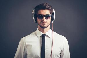 sentir sua batida. retrato de jovem bonito bem vestido em fones de ouvido, olhando para a câmera em pé contra um fundo cinza foto