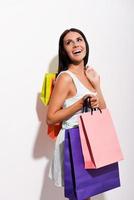 apreciando suas compras. excitada jovem de vestido carregando sacolas coloridas e olhando por cima do ombro com sorriso em pé contra um fundo branco foto