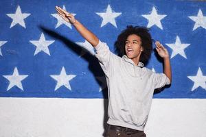 jovem e despreocupado. jovem africano em posar contra a bandeira americana e gesticular foto