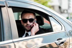 confiante e bem sucedido. sério jovem empresário falando no celular enquanto andava dentro de seu carro foto