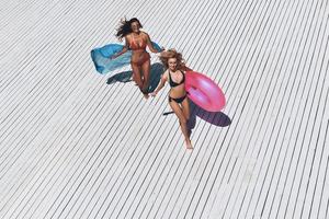 diversão de verão. vista superior de duas belas jovens de biquíni sorrindo enquanto corre ao ar livre foto