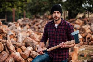 retrato da masculinidade. confiante jovem florestal segurando o machado e olhando para a câmera em pé ao ar livre foto