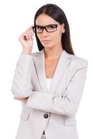 especialista em negócios confiante. bela jovem empresária de terno ajustando os óculos e olhando para a câmera em pé contra um fundo branco foto