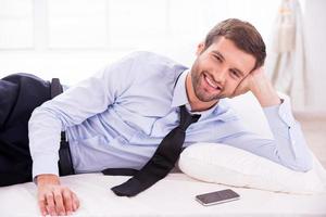 empresário relaxante. jovem bonito de camisa e gravata, deitado na cama e sorrindo foto