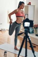comprimento total de jovem flexível em roupas esportivas se aquecendo antes do treinamento enquanto faz vídeo de mídia social foto