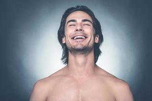 sentindo tão feliz. retrato de jovem sem camisa olhando para a câmera e sorrindo em pé contra um fundo cinza foto