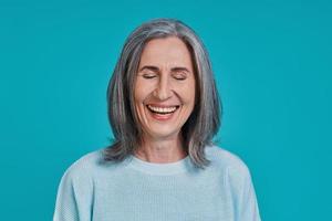 tiro na cabeça de mulher bonita madura rindo em pé contra um fundo azul foto