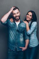 parecendo ótimo e se sentindo feliz. tiro de estúdio do lindo casal jovem em jeans usam de pé perto um do outro e olhando para a câmera com um sorriso foto