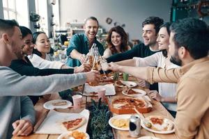 grupo de jovens em roupas casuais escolhendo pizza e sorrindo enquanto faz um jantar dentro de casa foto