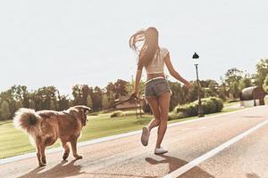 amigos para sempre. vista traseira de corpo inteiro de jovem brincando com seu cachorro enquanto corre ao ar livre foto