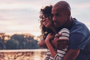 casal romantico. feliz casal jovem abraçando e sorrindo enquanto está sentado no cais perto do lago foto