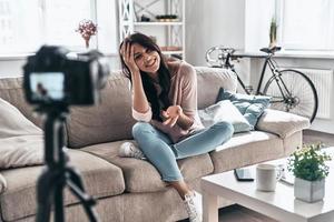 linda blogueira. vlogger feminina fazendo vídeo de mídia social e sorrindo enquanto está sentado dentro de casa foto