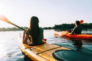 curtindo a aventura no rio juntos. vista traseira do belo casal jovem andando de caiaque no lago juntos foto