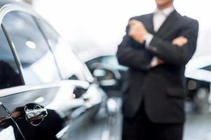 escolhendo um carro na concessionária. homem de cabelo grisalho pensativo em trajes formais, inclinando-se para o carro e desviando o olhar foto