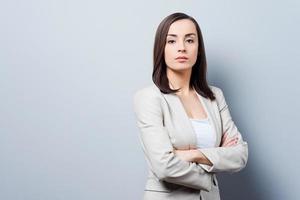 empresária encantadora. confiante jovem empresária mantendo os braços cruzados e olhando para a câmera em pé contra um fundo cinza foto