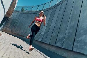 comprimento total de mulher jovem e bonita em roupas esportivas correndo ao ar livre foto