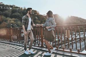 totalmente apaixonado. comprimento total de homem bonito olhando para uma jovem mulher atraente e sorrindo em pé na ponte ao ar livre foto