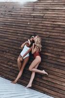 comprimento total de mulher jovem e atraente em trajes de banho beijando sua amiga enquanto posava contra a parede de madeira ao ar livre foto