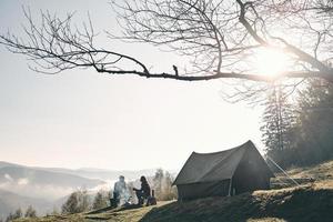 manhã de sol. jovem casal tomando café da manhã enquanto acampa nas montanhas foto