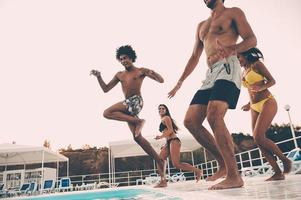 pronto para pular. grupo de jovens bonitos olhando felizes enquanto pulavam para a piscina juntos foto