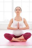 exercícios de relaxamento. linda mulher grávida mediando e mantendo os olhos fechados enquanto está sentado em posição de lótus foto