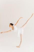 habilidade e graça. vista lateral de comprimento total da bela jovem bailarina em tutu branco dançando contra fundo branco foto