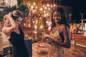 duas mulheres bonitas em vestidos de noite dançando e sorrindo enquanto passam o tempo na festa de luxo foto