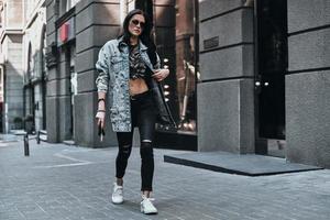 moda é a vida dela. comprimento total de jovem atraente ajustando sua jaqueta jeans enquanto caminhava na rua foto