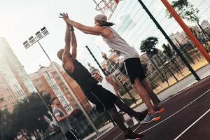 vitória dois jovens em roupas esportivas dando uns aos outros cinco em um símbolo de vitória enquanto jogava basquete com amigos ao ar livre foto